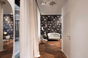 A modern interior with a herringbone wood floor, a white sofa, and a floral wallpaper. - Agorà - Boutique Stays (Turin)