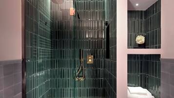 Uma casa de banho moderna com chuveiro em cabine de vidro, uma banheira branca e uma estante com produtos de higiene pessoal.