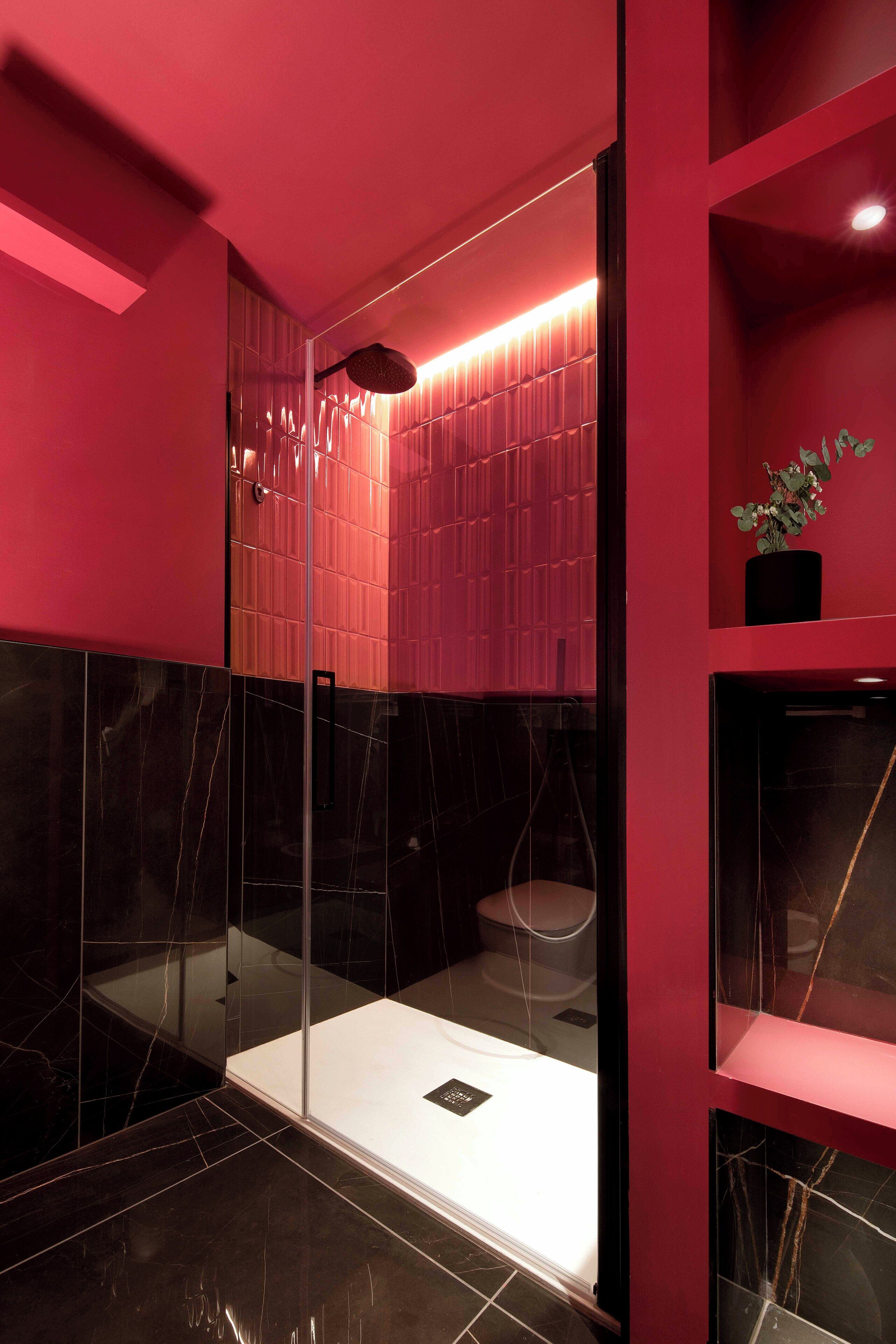 A modern bathroom with a glass enclosure, a white sink, and a red accent wall.