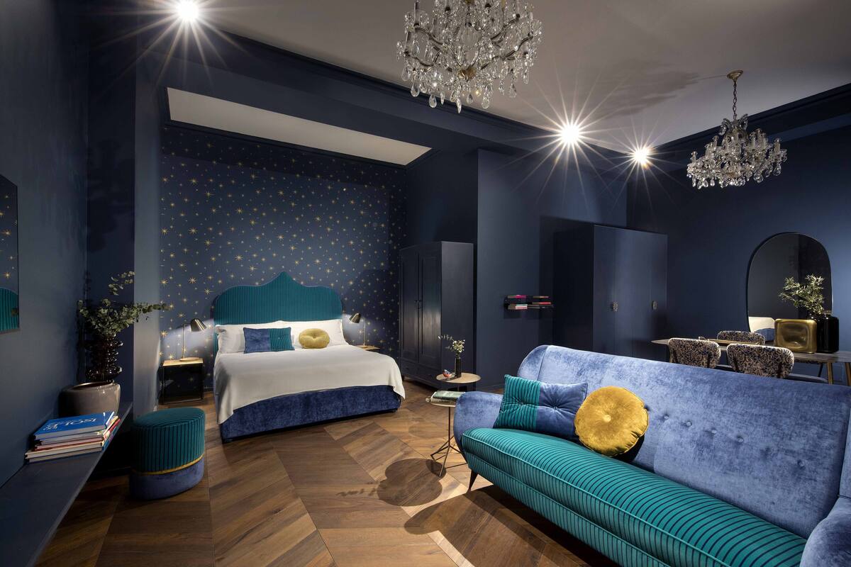 A modern bedroom with a large bed, a sofa, a chandelier, and a starry wall.