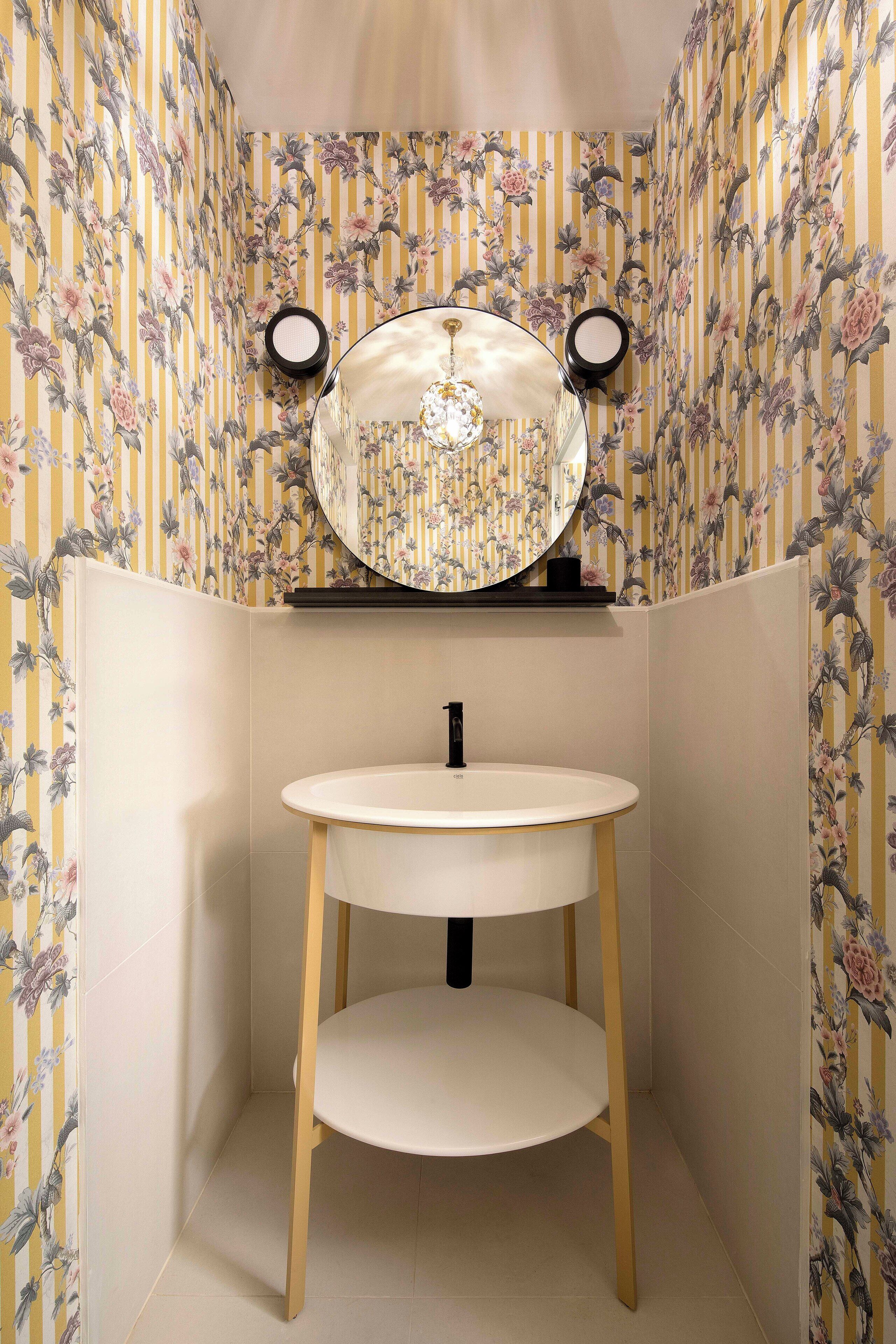 Une petite salle de bain d’angle avec un miroir rond, un lavabo blanc et des pieds en bois.