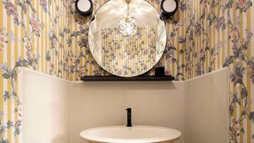Une petite salle de bain d’angle avec un miroir rond, un lavabo blanc et des pieds en bois.