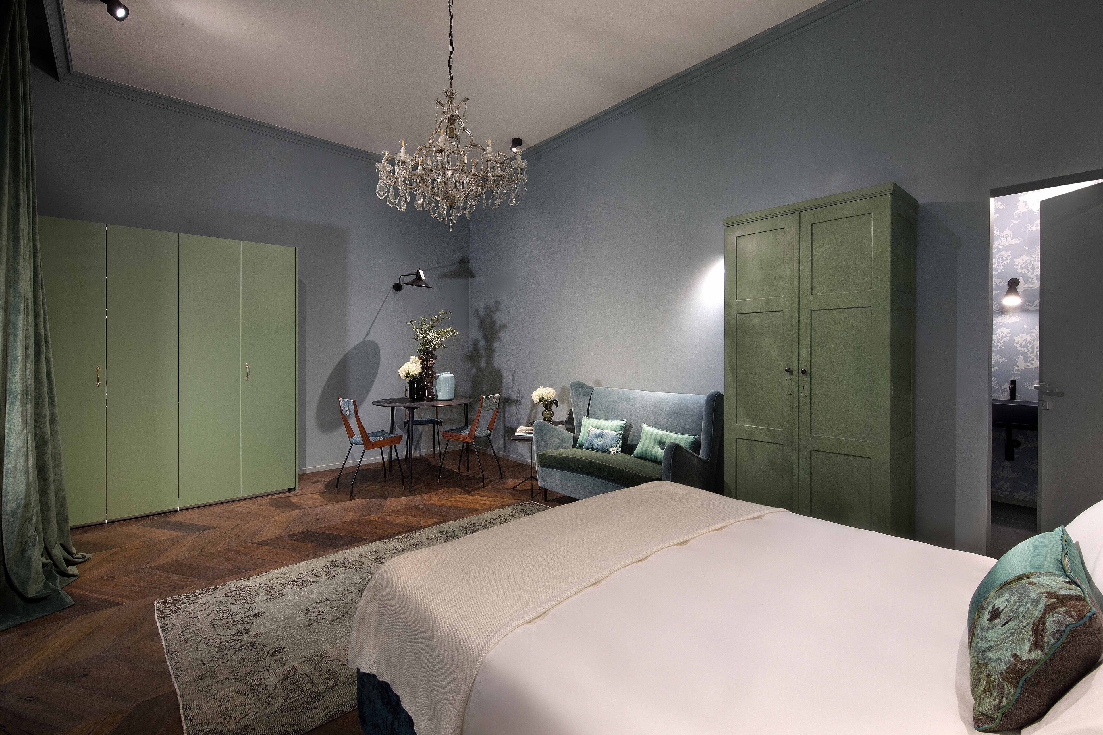 Een slaapkamer met een groot bed, een groene garderobe, een groene bank, een kroonluchter en een kleine tafel met stoelen.