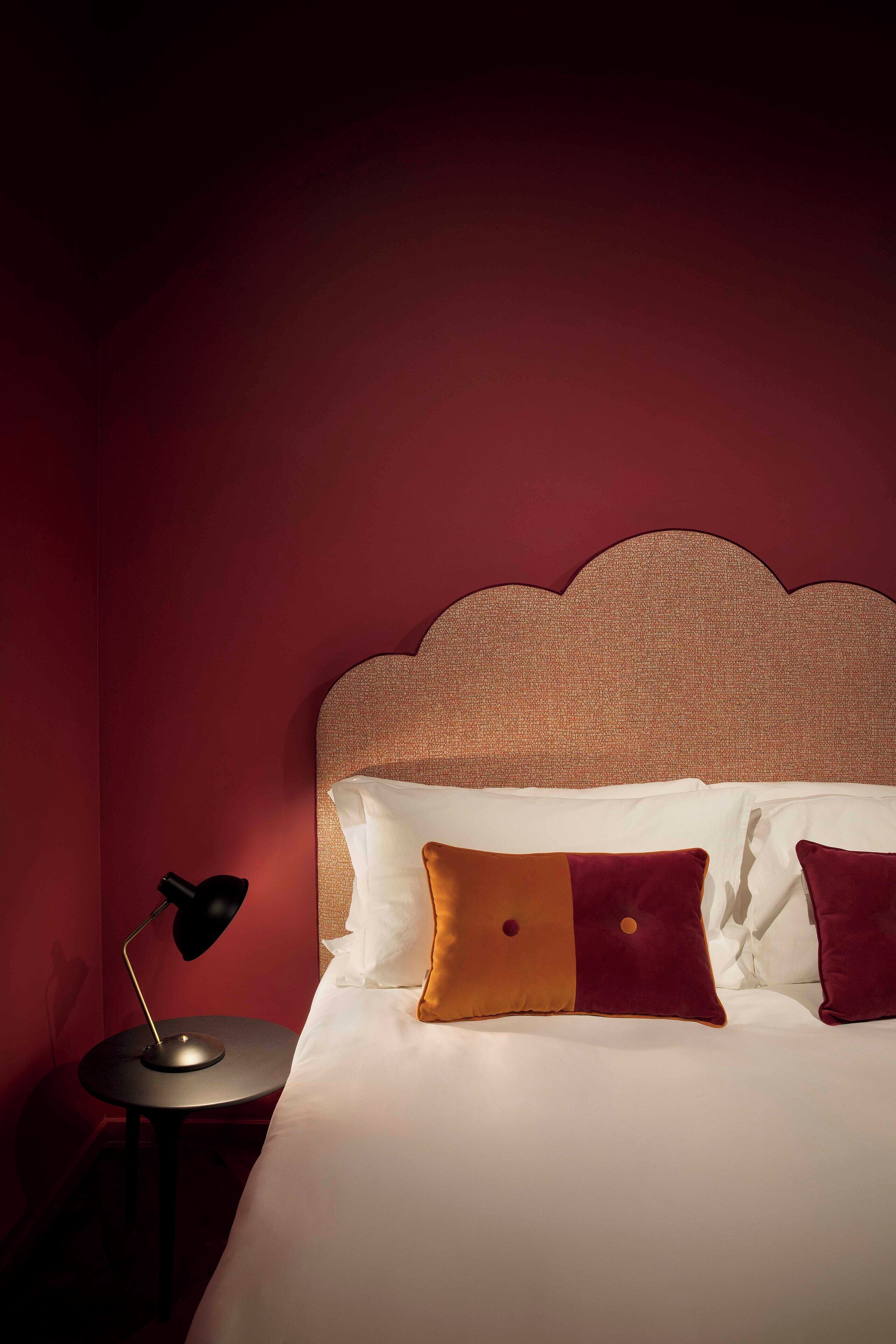A neatly made bed with a headboard, a bedside table with a lamp, and a wall with a textured pattern.