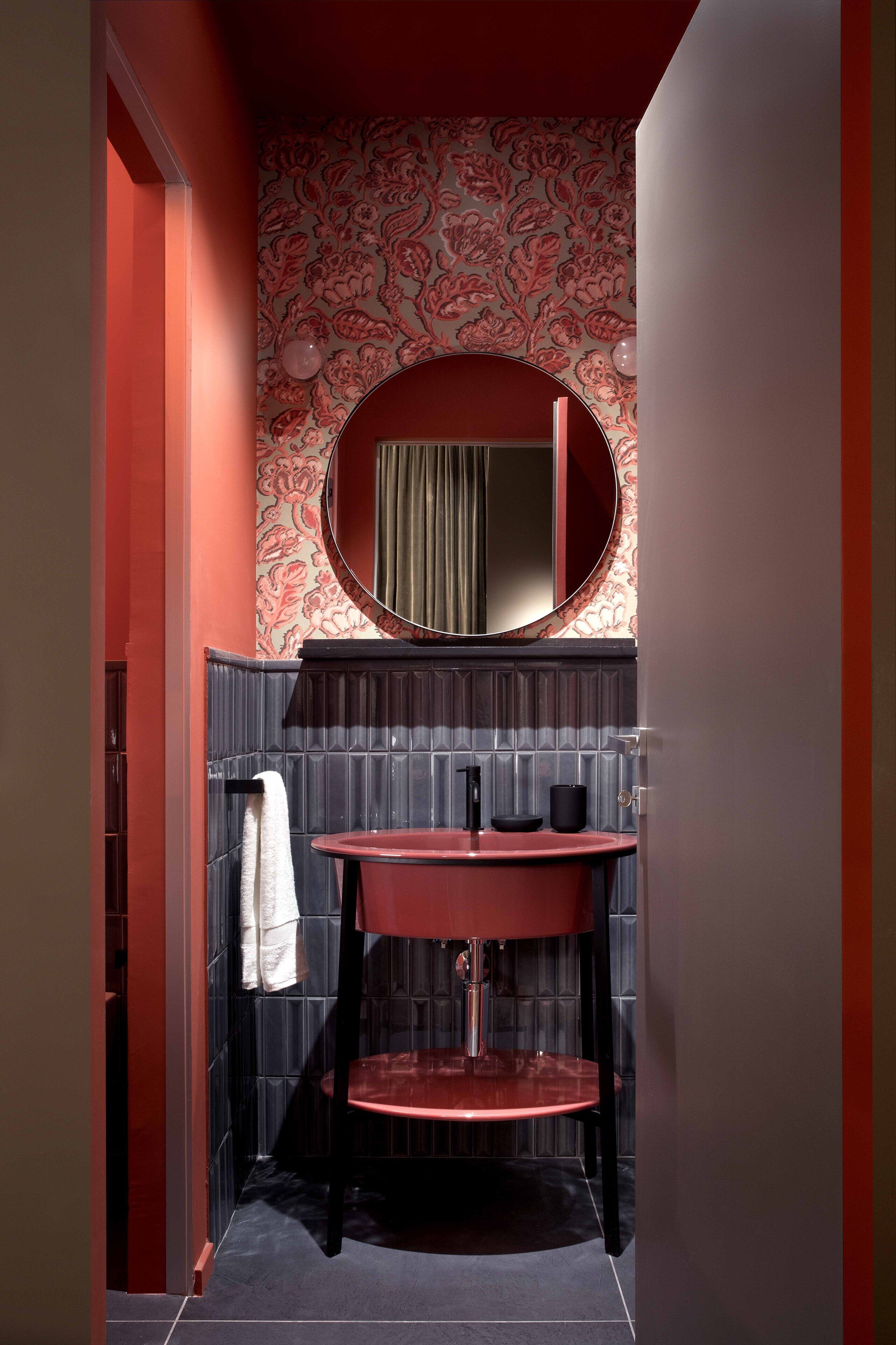 Ein Badezimmer mit einem roten Waschbecken, einem Spiegel und einer Wand mit Muster.