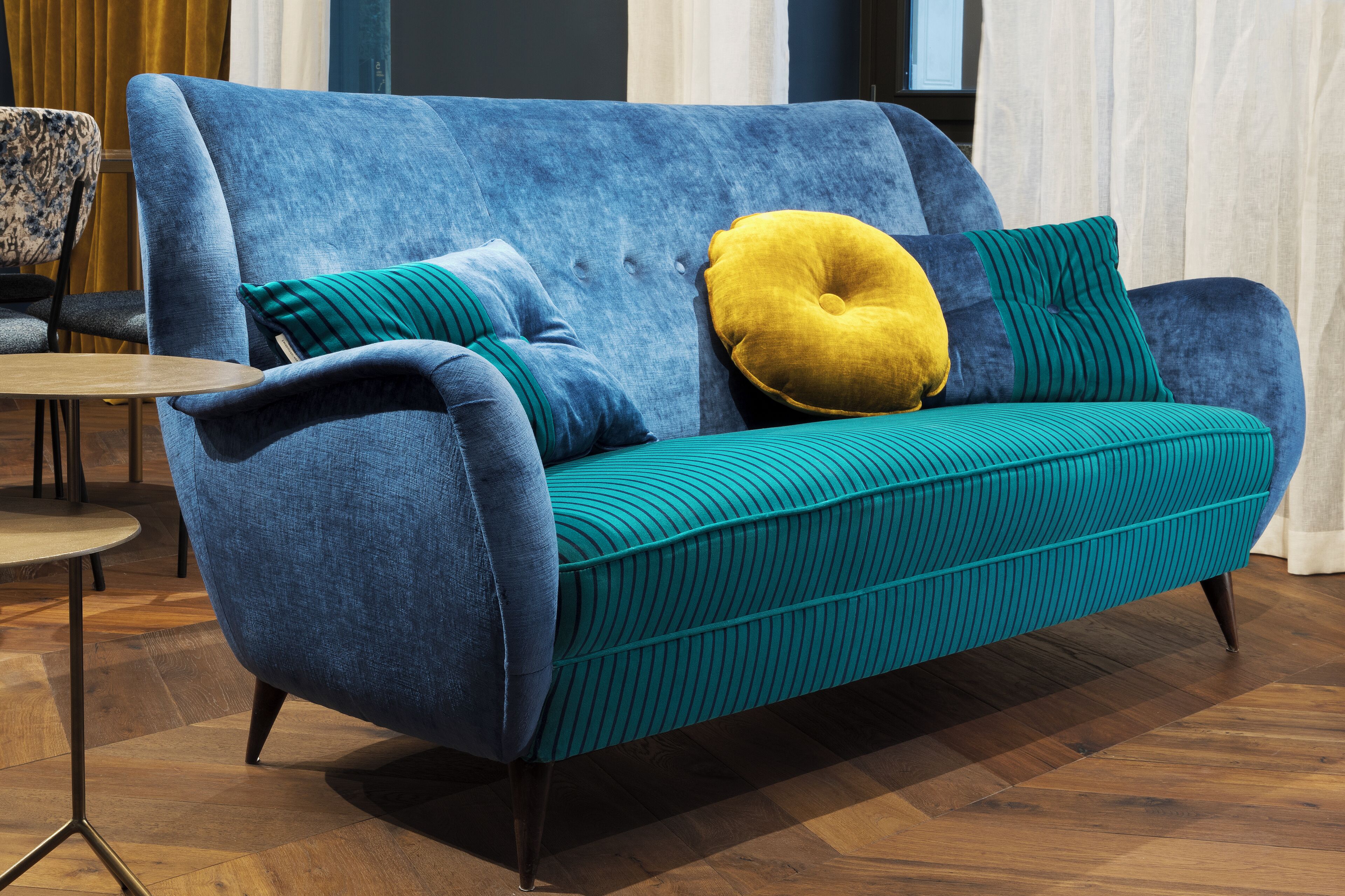 A blue sofa with teal cushions and a yellow accent pillow in a modern room with wooden flooring and a small table.