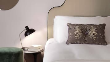 A neatly arranged bedroom with a large bed, a round mirror, a small side table, and a green ottoman.