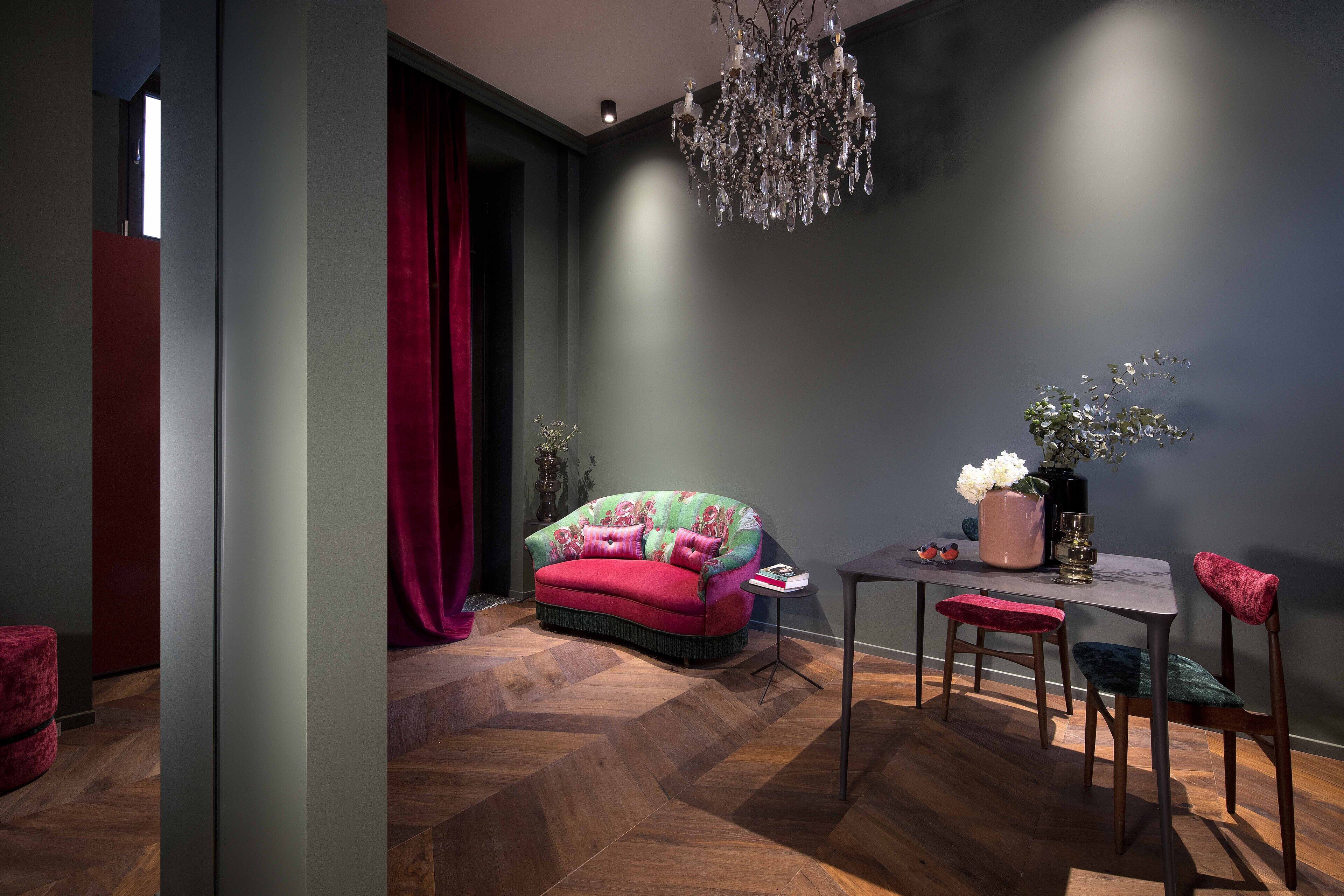A modern room with a herringbone wood floor, a red sofa, a dining table with chairs, and a chandelier.