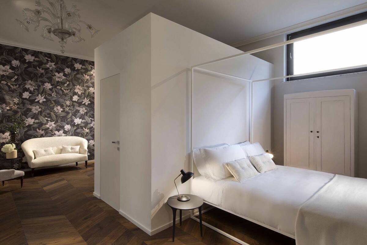 A bedroom with a bed, a nightstand, a wardrobe, a sofa, and a floral wallpaper.