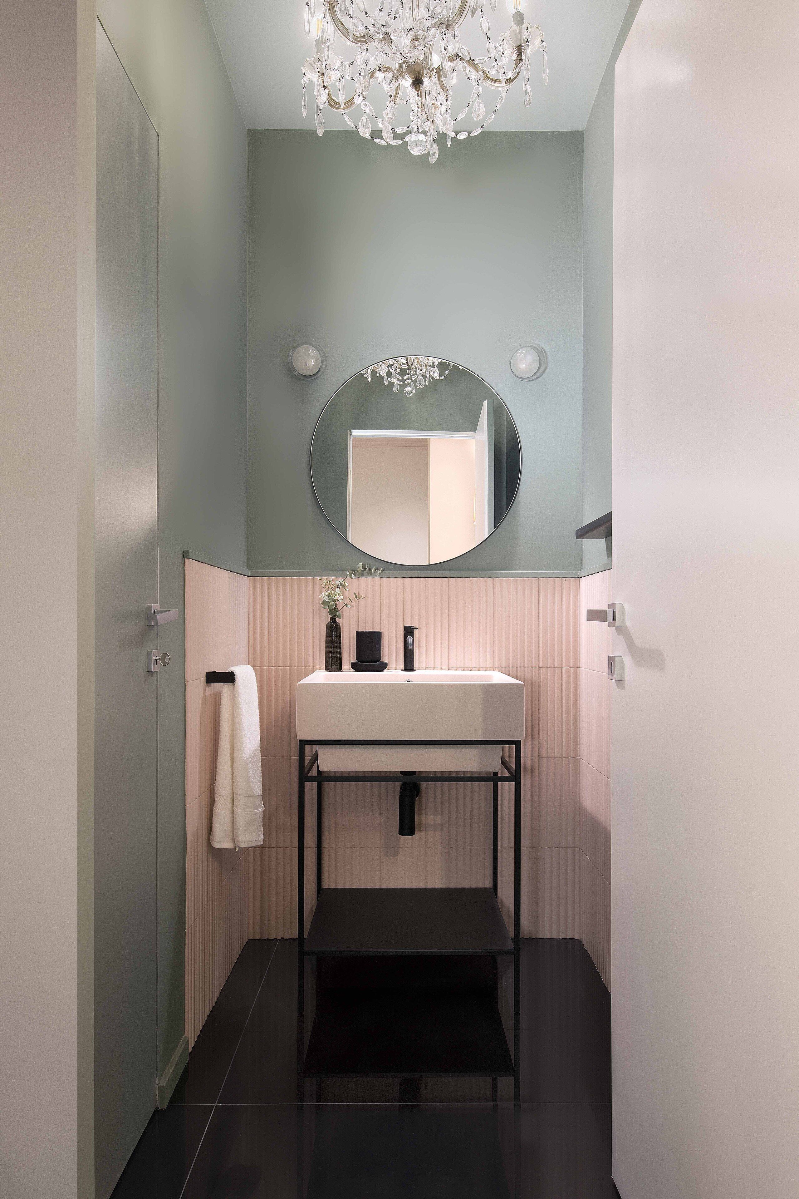 Une salle de bain moderne avec un lavabo blanc, un miroir rond et un lustre.