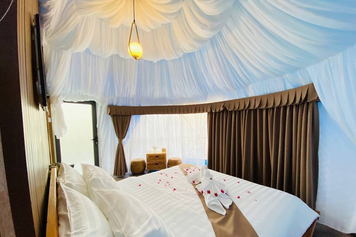 Une chambre d’hôtel avec un grand lit, une table de chevet, une lampe et des rideaux.