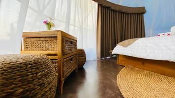 Una habitación con una cama, un aparador de madera y otomanas tejidas.