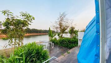 A view from inside a tent overlooking a lakeside area with a table and chairs, surrounded by greenery.