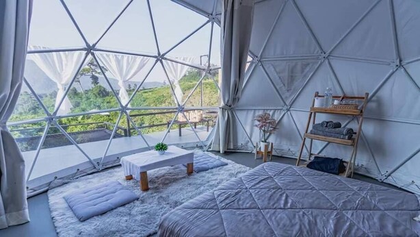 Quarto espaçoso com uma cama grande, uma mesa pequena e uma estante com objetos.