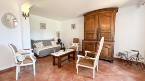 Una habitación con un sofá, dos sillas, un armario de madera y una bicicleta.