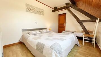 A bedroom with a wooden sloped ceiling, a bed with a quilt, a chair, and a wooden door.