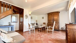Una sala acogedora con un sofá, dos sillas blancas, un aparador de madera y una mesa de comedor.