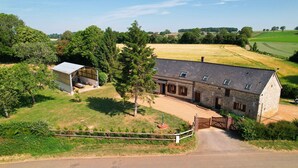 Una casa de campo de piedra con un granero, rodeada de campos y árboles.