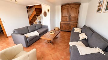 Ein Wohnzimmer mit zwei grauen Sofas, einem Holztisch, einem beigen Sessel und einer Treppe, die zu einer oberen Etage führt.