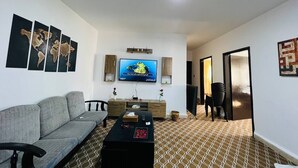 A living room with a grey sofa, a coffee table, a flat-screen TV, and patterned flooring. - Petra Triclinium Home (Wadi Musa)