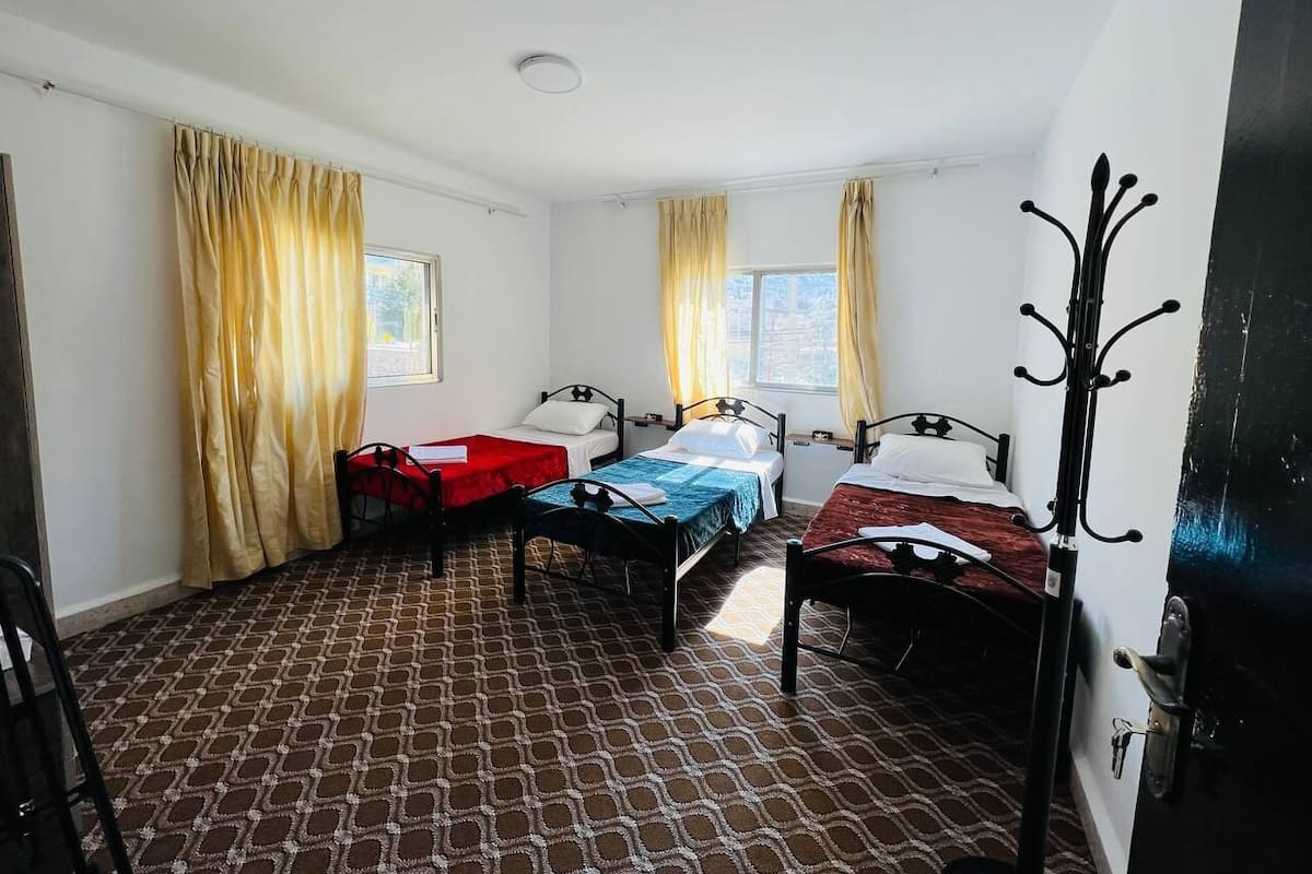 A room with three beds, a red table, and a black coat rack.