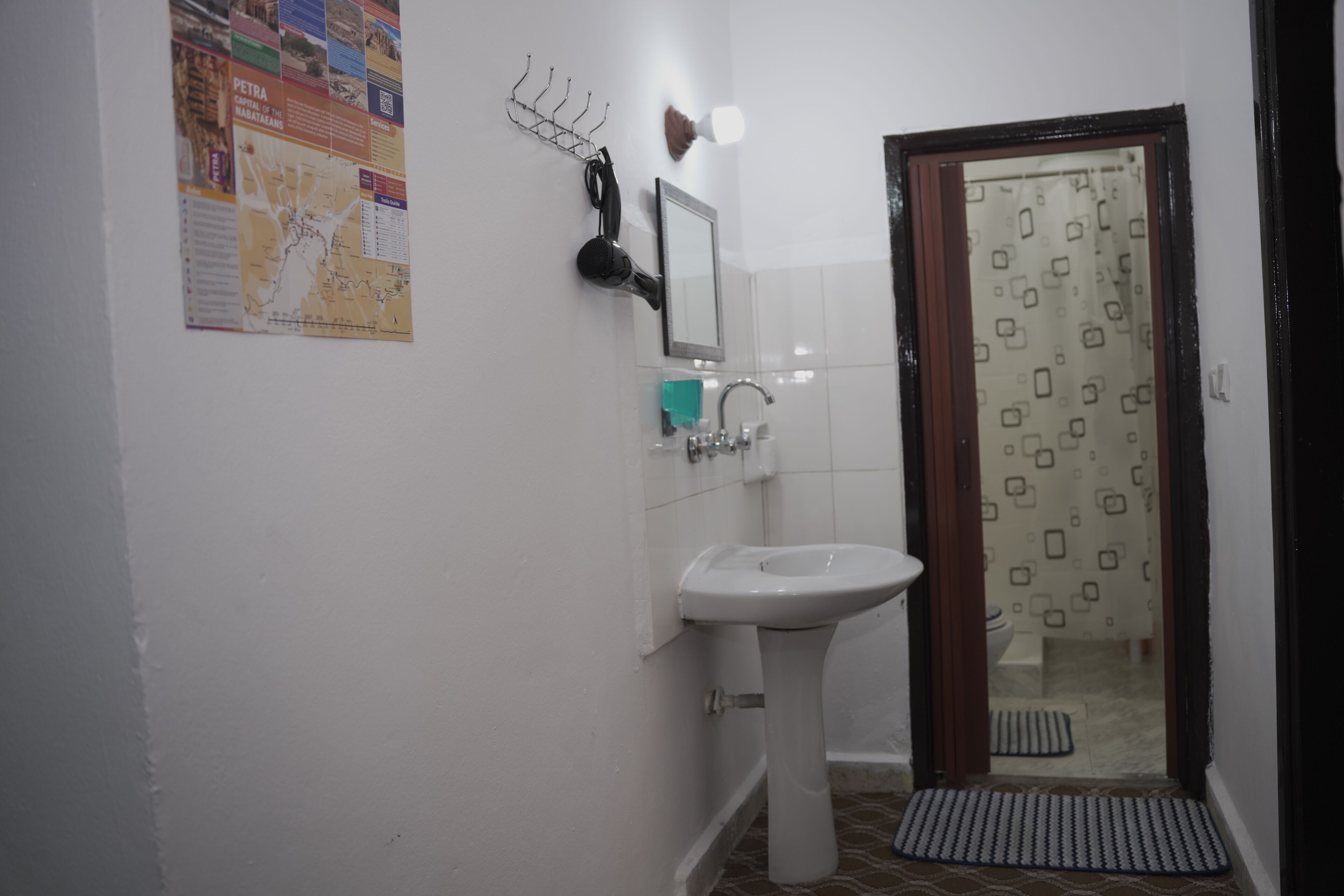 A bathroom with a white sink, a mirror, a map on the wall, and a shower area with a patterned curtain.