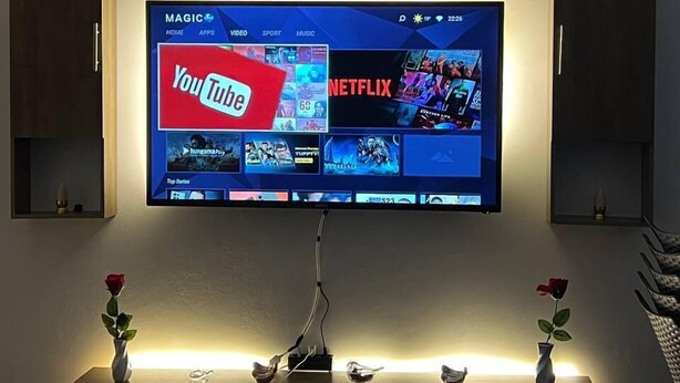 A flat-screen TV mounted on a wall with a wooden shelf above it. - Petra Triclinium Home (Wadi Musa)