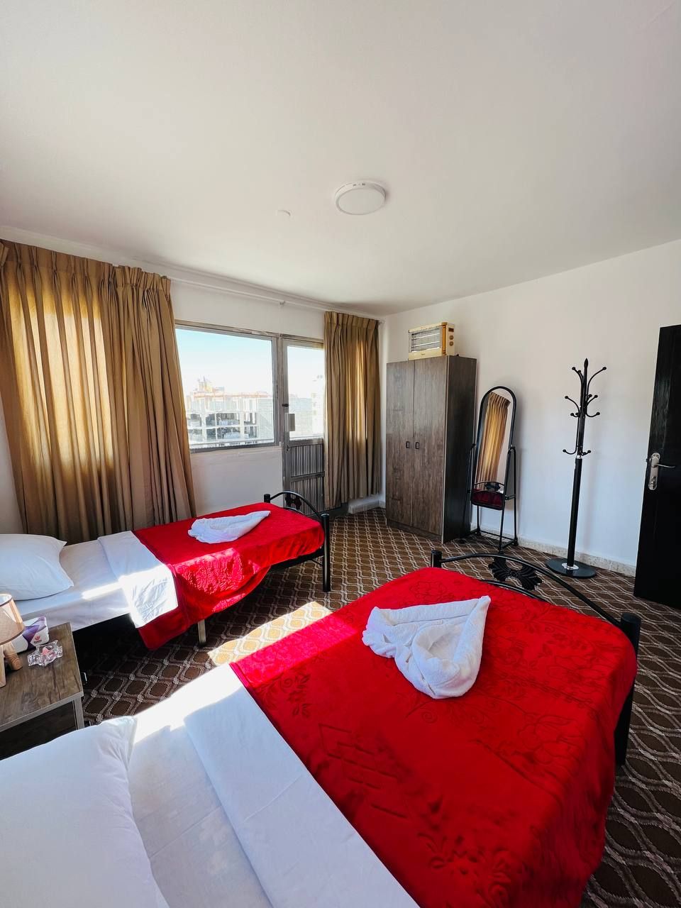 A hotel room with two beds, a wardrobe, a coat rack, and a window with curtains.
