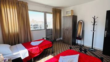 A hotel room with two beds, a wardrobe, a coat rack, and a window with curtains.
