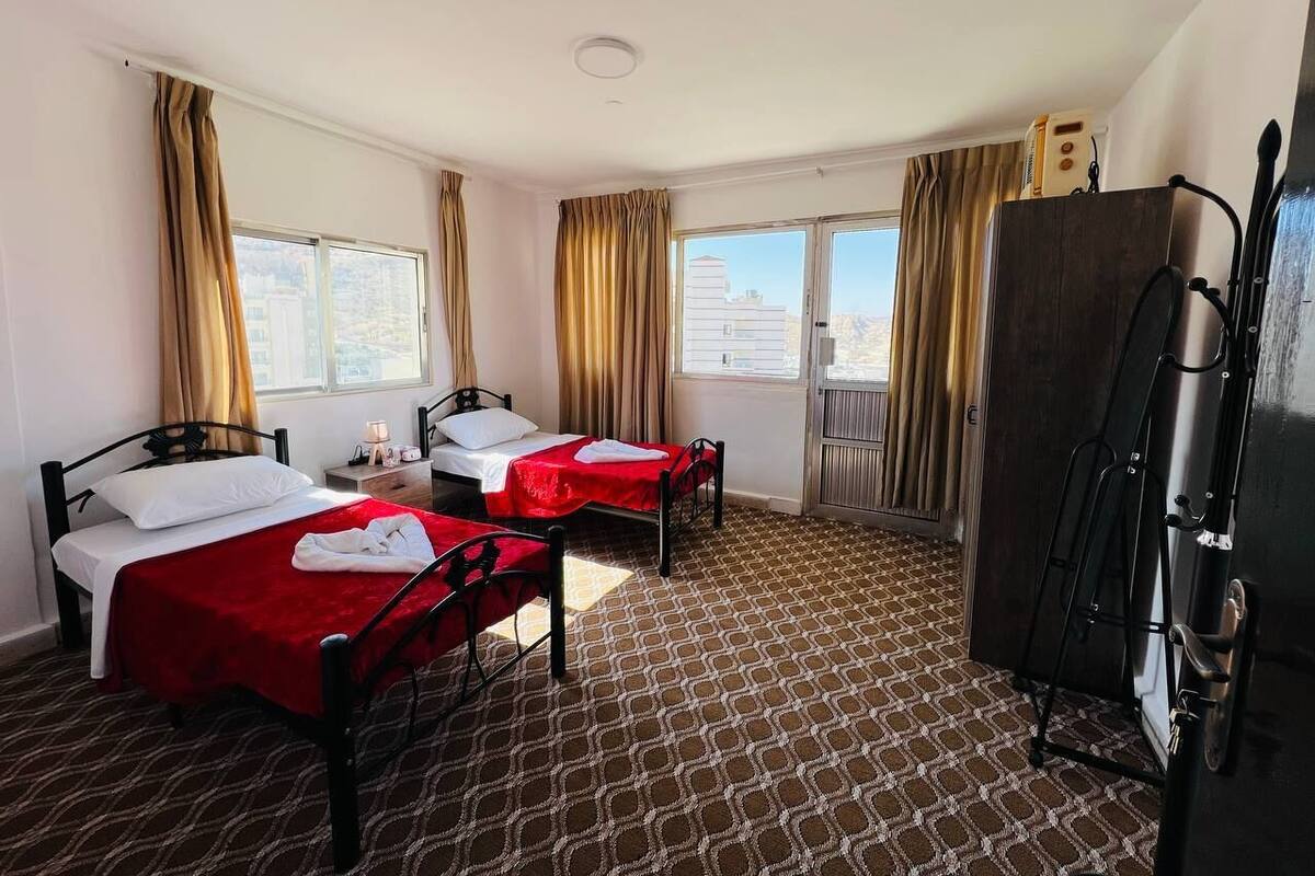 A hotel room with two beds, a wardrobe, and a large window.
