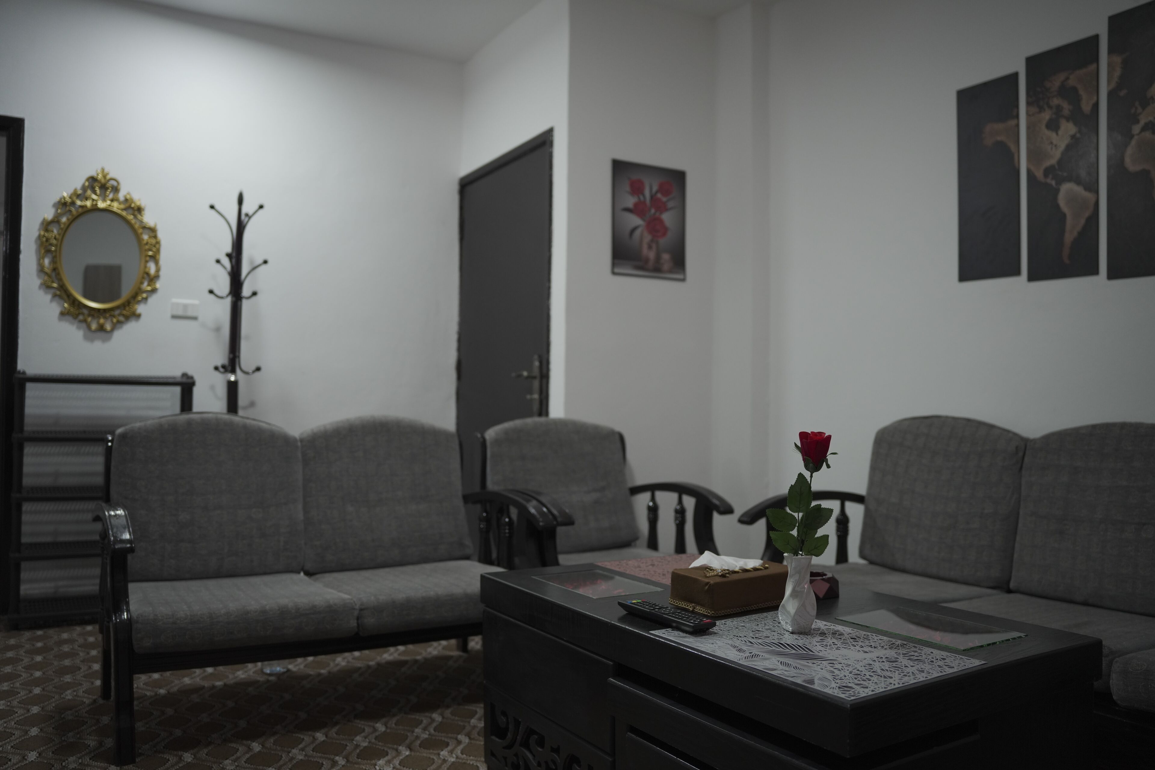 A living room with a sofa, a coffee table with a vase and a rose, a coat rack, and a mirror on the wall.