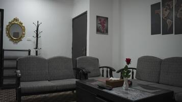 A living room with a sofa, a coffee table with a vase and a rose, a coat rack, and a mirror on the wall.