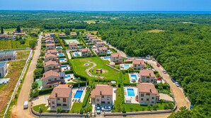 An aerial view of a residential area with multiple houses, a central swimming pool, and a road. - Villa LiLi Apt 3 Studio (Poreč)