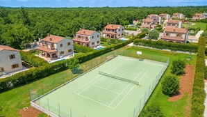 A tennis court surrounded by residential buildings with a green landscape in the background. - Villa LiLi Apt 3 Studio (Poreč)