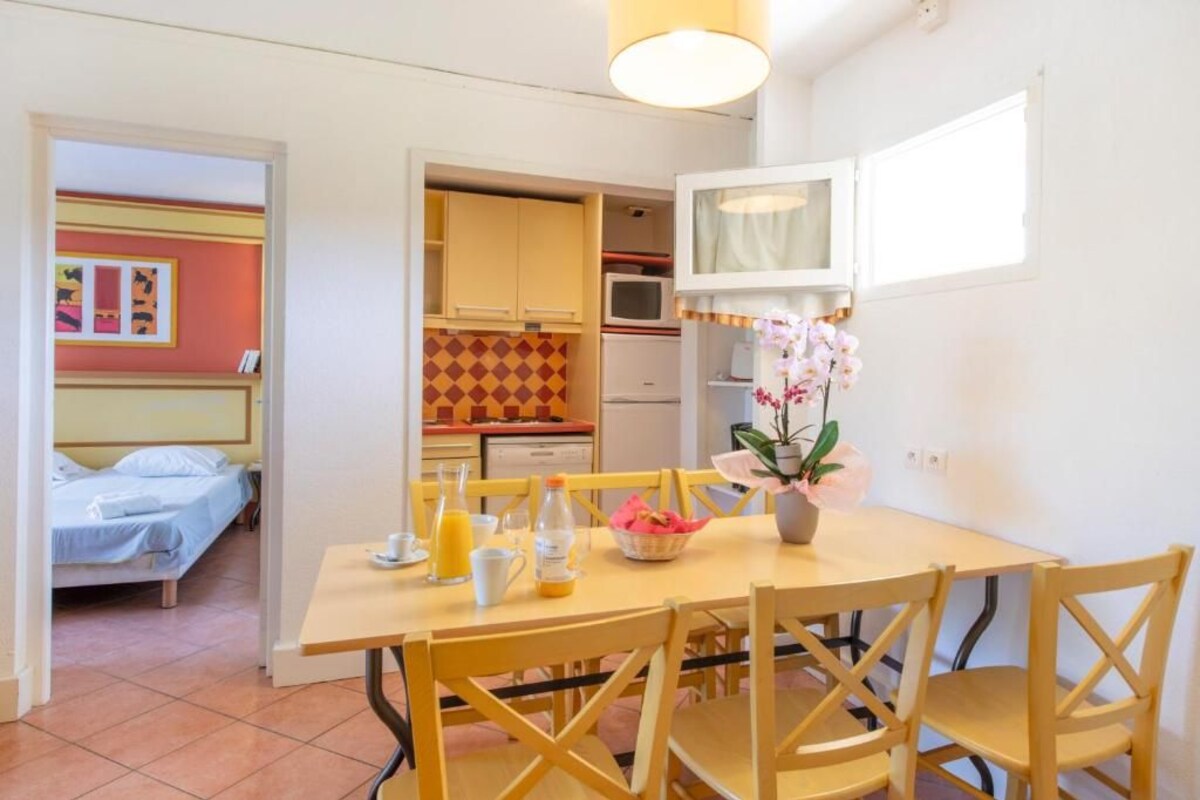A compact hotel room with a dining area, a kitchenette, and a bed.