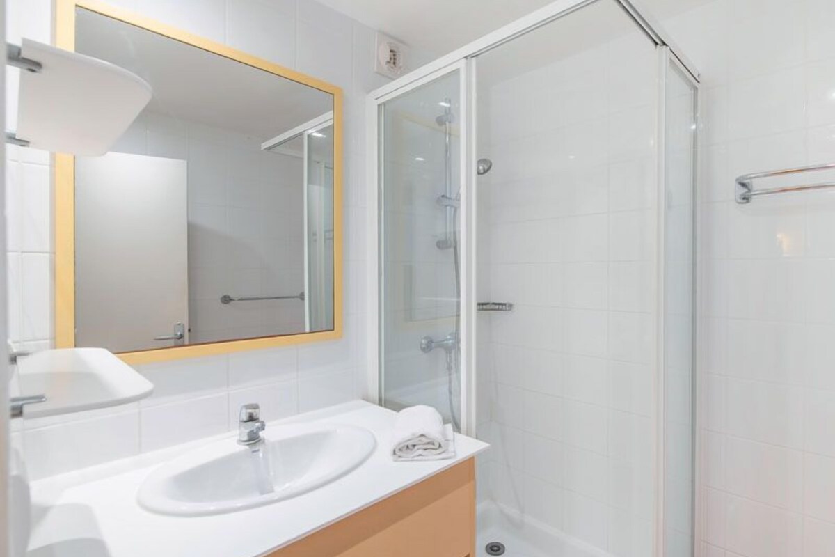 A modern bathroom with a white sink, mirror, and glass shower enclosure.