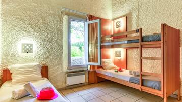 Ein Zimmer mit einem Etagenbett, einem Einzelbett, einem Fenster mit Vorhängen, einer Wandleuchte und einem Heizkörper.