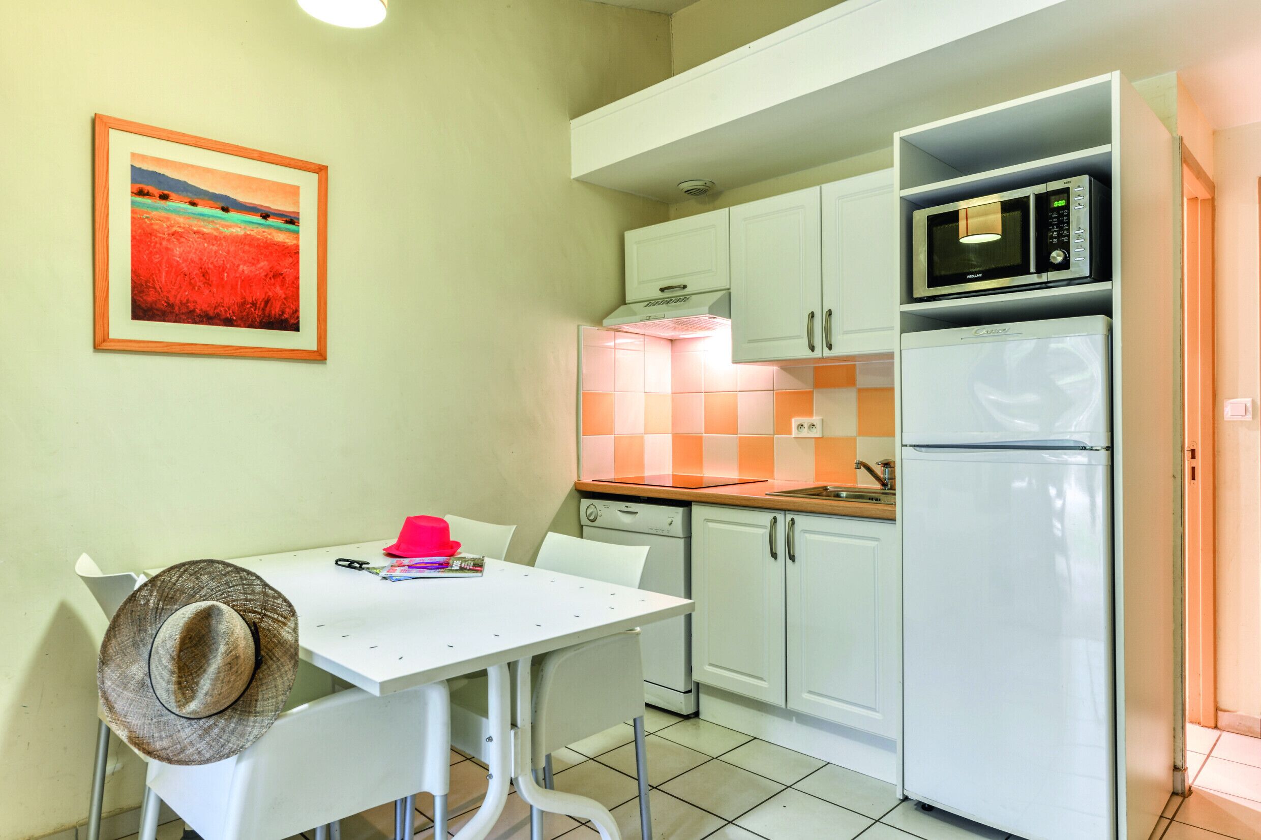 A kitchen with white cabinets, a microwave, a refrigerator, and a dining table with chairs.