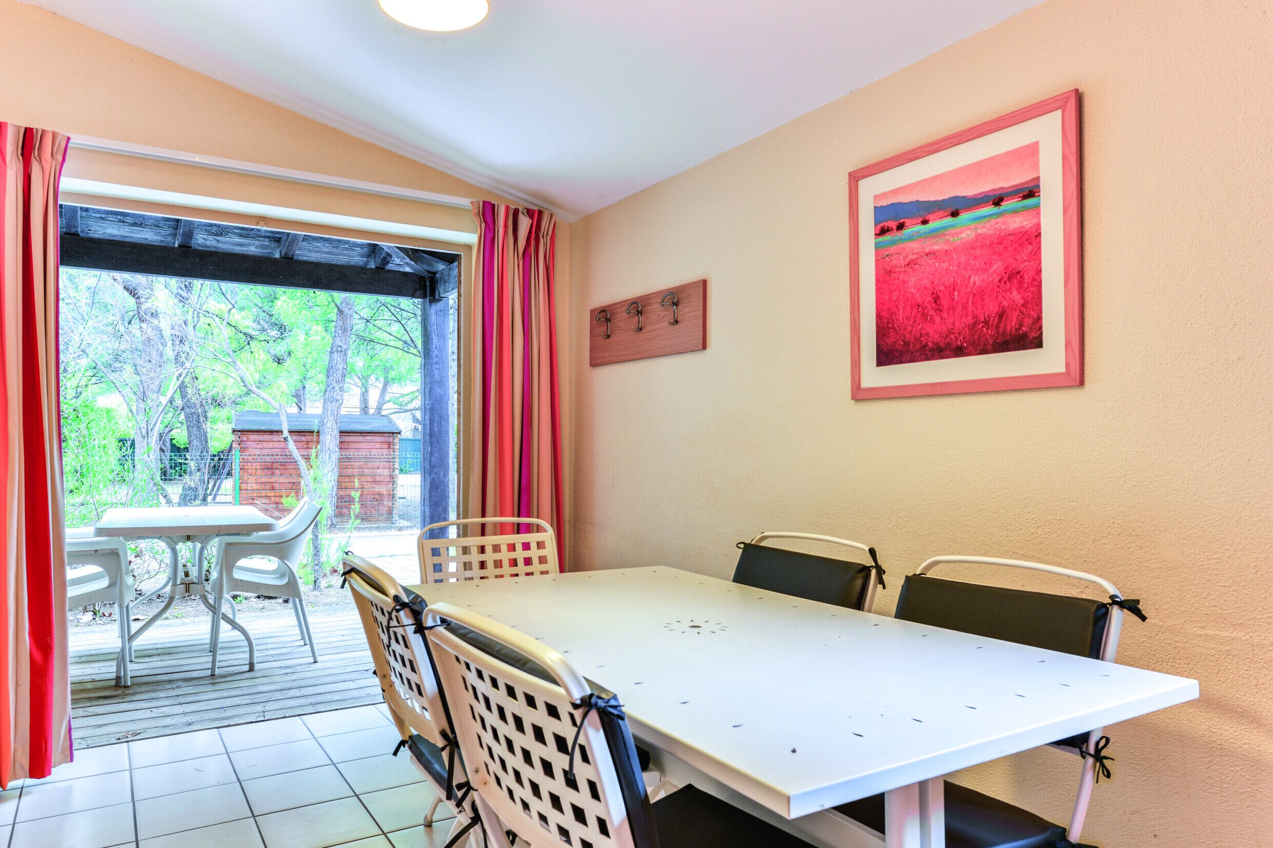 Un comedor con una mesa y sillas, vista a través de un ventanal y un cuadro en la pared.