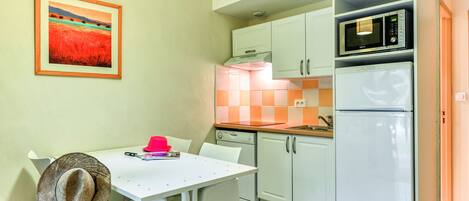 A kitchen with white cabinets, a microwave, a refrigerator, and a dining table with chairs.