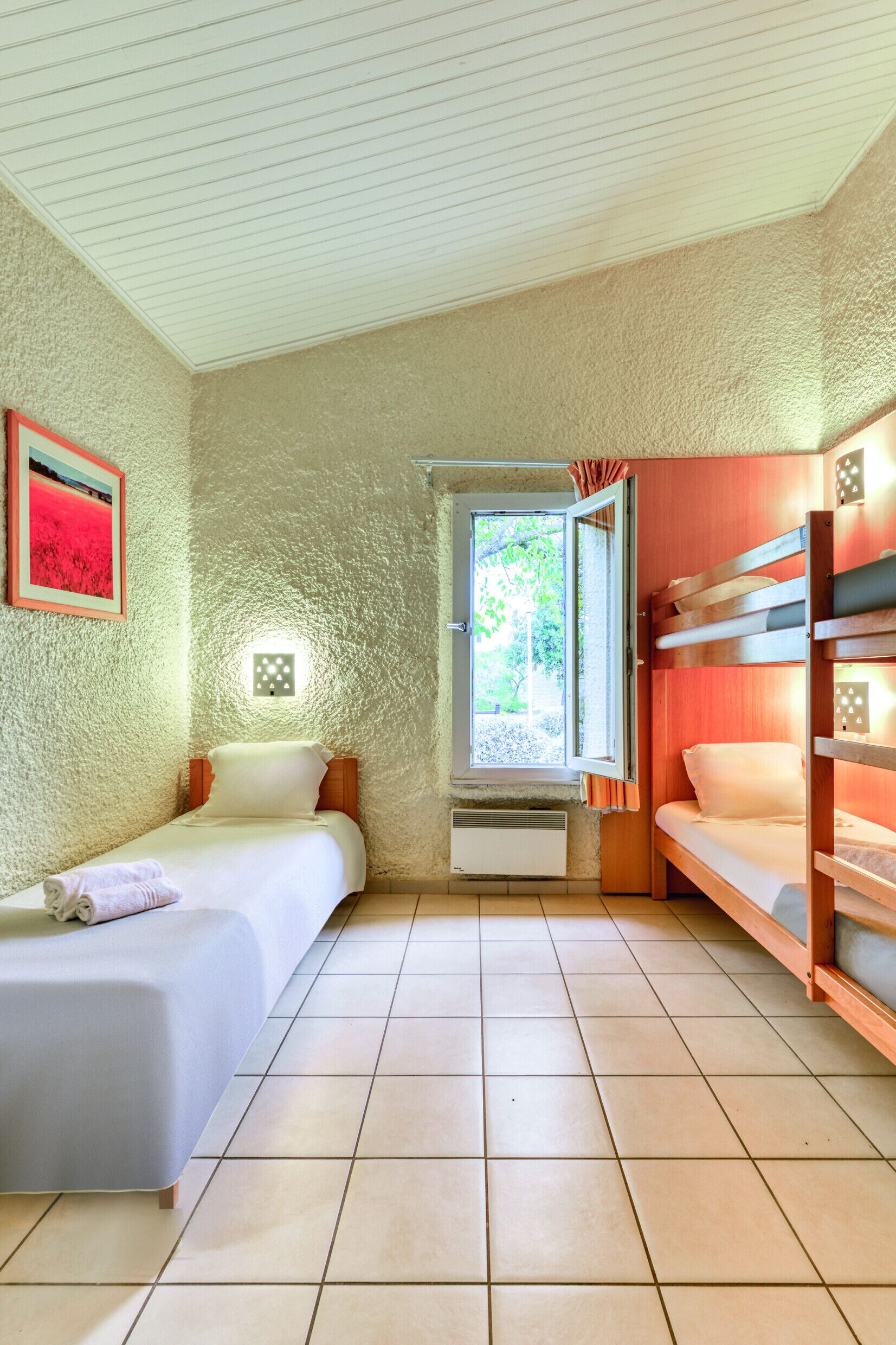 A compact room with a single bed, a window with curtains, a small wall-mounted light, and a bunk bed.