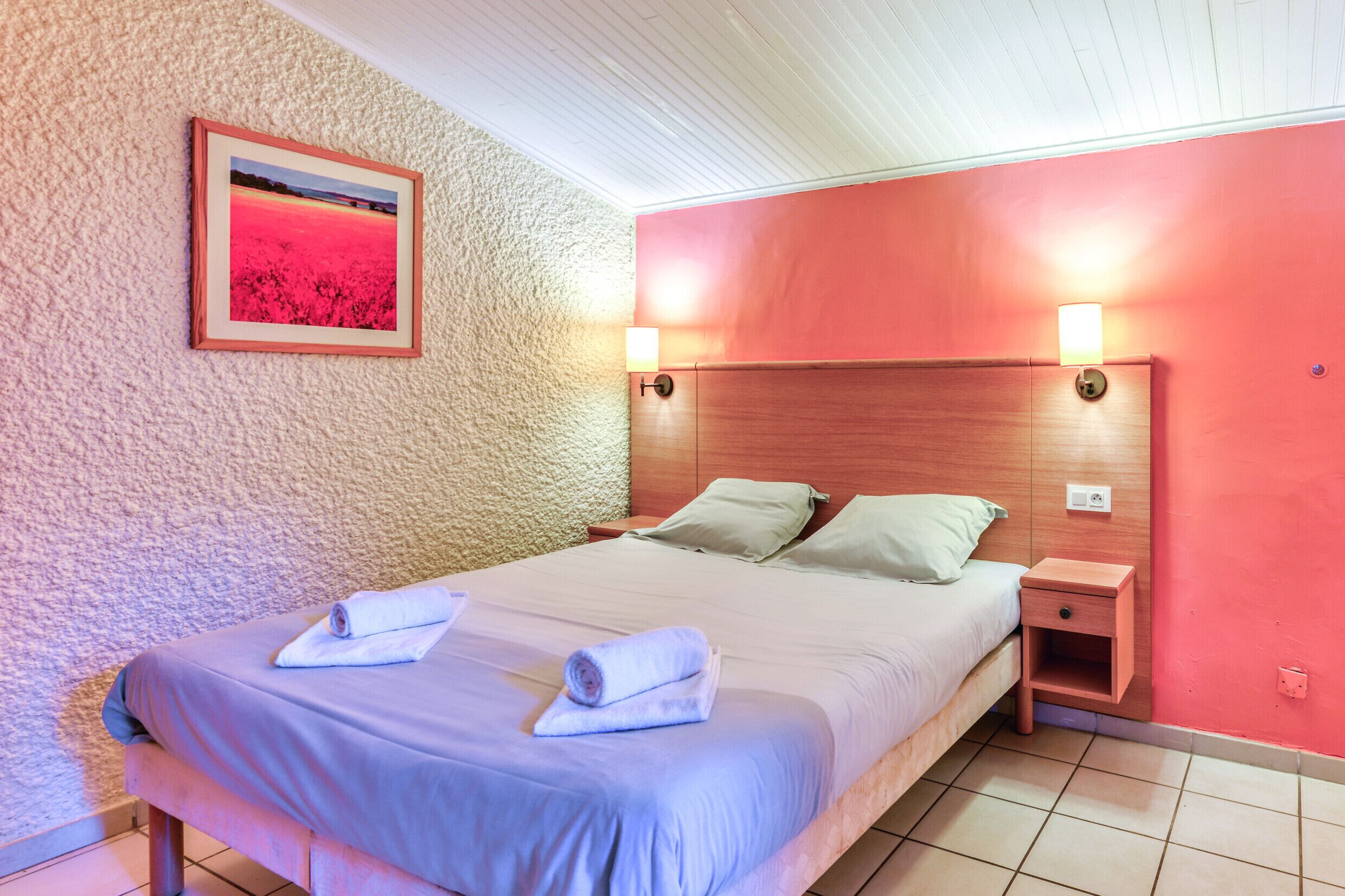 Un lit bien fait, avec des serviettes, une tête de lit en bois et une petite table de chevet avec une lampe.