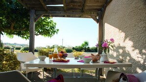 An outdoor dining area with a table set for breakfast, surrounded by chairs, and a view of the landscape. - SOWELL RESIDENCES Les Lauriers Roses (Agde)