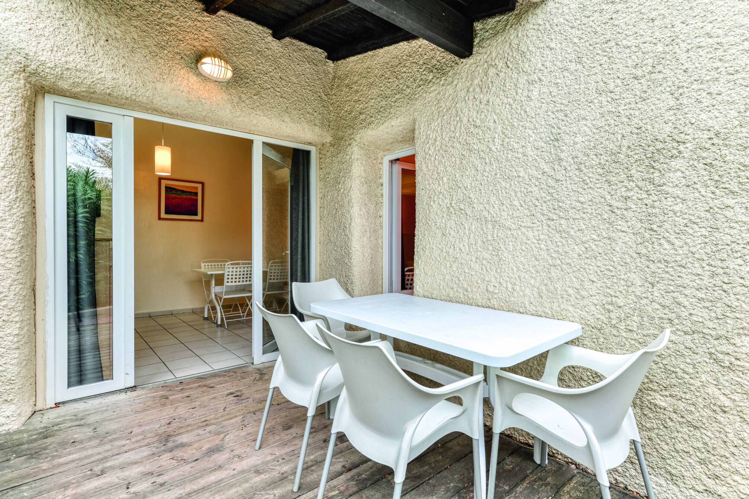 Un patio con mesa y sillas blancas, una puerta corrediza de vidrio y una pared con textura.