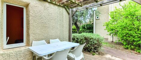 Un patio cubierto con mesa y sillas, una ventana y vista a follaje.