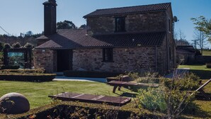Un edificio de piedra con tejado de baldosas, una chimenea y un pequeño jardín con piscina y zona de estar.