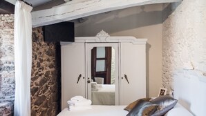 Un dormitorio con pared de piedra, un armario blanco, una cama con ropa de cama blanca y una almohada marrón.