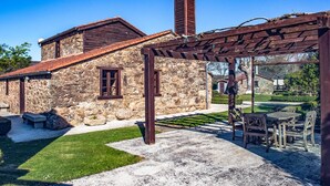Un edificio de piedra con techo de madera, una pérgola y un césped bien cuidado.