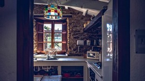 Una cocina con pared de piedra, armarios de madera, un ventanal de vidrio emplomado de colores y un refrigerador blanco.