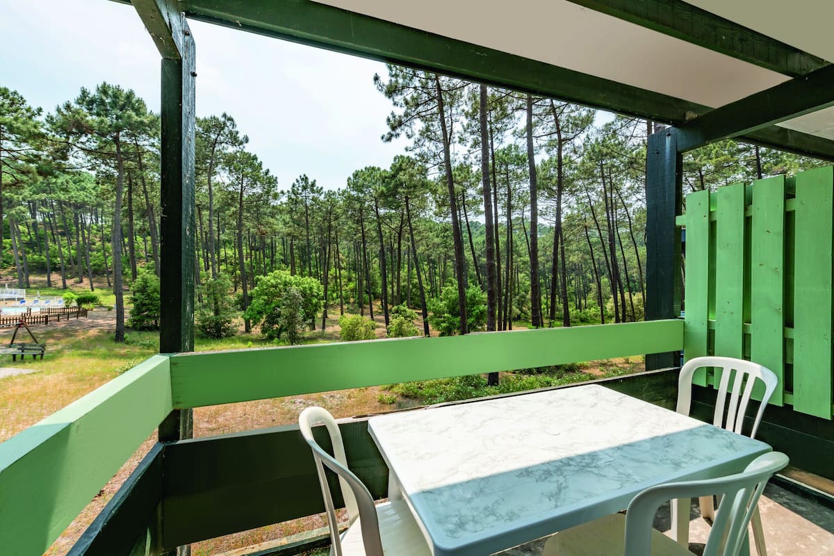 A covered outdoor seating area with a table and chairs, overlooking a forest.